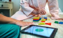 A therapist and an older patient with cognitive impairment, shot from the chest down, play with building blocks and a digital tablet,
